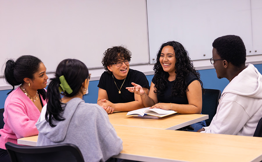 Lirio smiles and leads a group discussion at a classroom table with four attentive students.